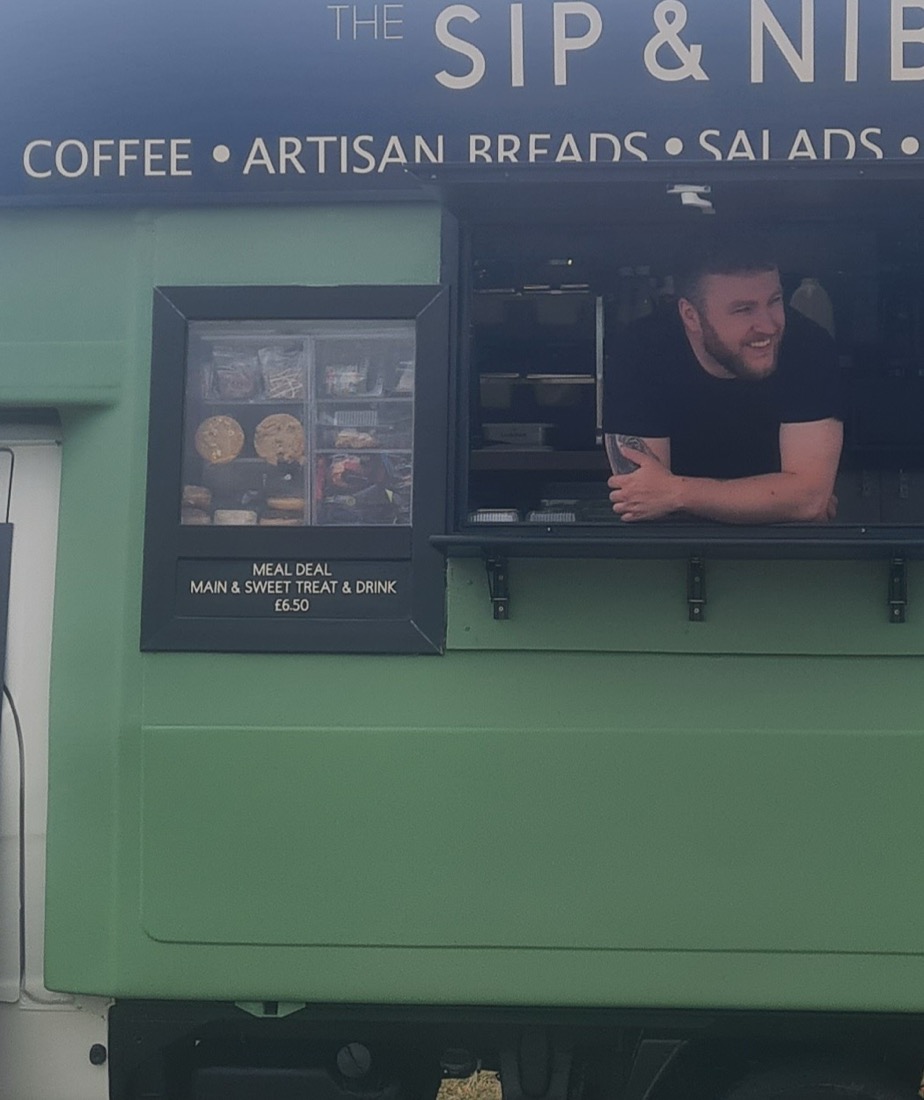 A smiling barista serving from the Sip & Nibble van hatch